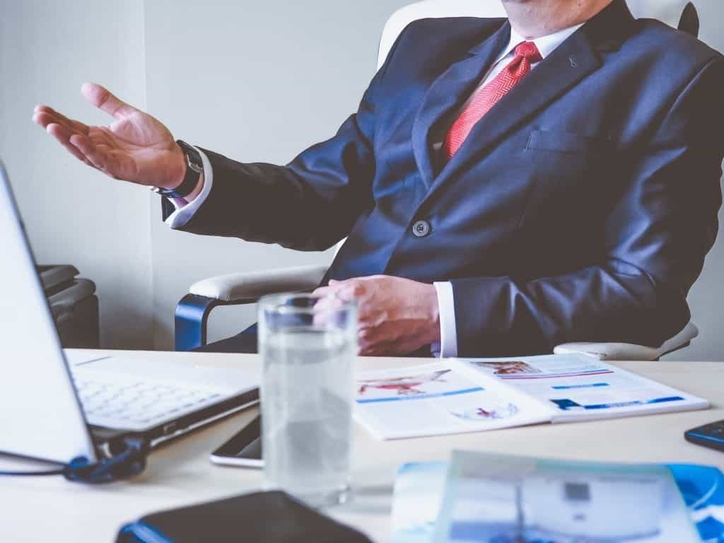 An anonymous businessman sits behind his office desk, gesturing with hands.