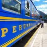 A blue Perurail train at an outdoor train station on a sunny day.