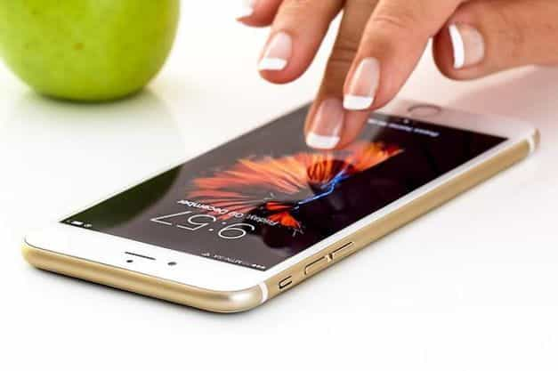 A smartphone lying down flat on a desk with a hand about to tap on its screen.