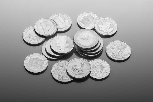 A collection of silver coins of different currencies lying on a table, some showing heads and other tails, with some stacked on top of one another while others lay around alone.