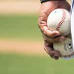 A pitcher during a game of baseball holding two baseballs together in their left hand.