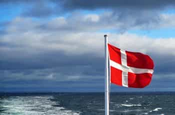 A flag on a pole near the sea under a cloudy sky.